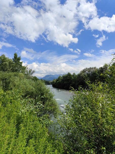 Ein lebhafter Fluss fließt zwischen grünen Ufern unter einem wolkigen Himmel.