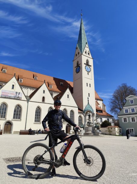 Junger Mann auf einem Fahrrad vor einem historischen Gebäude mit Kirchturm.