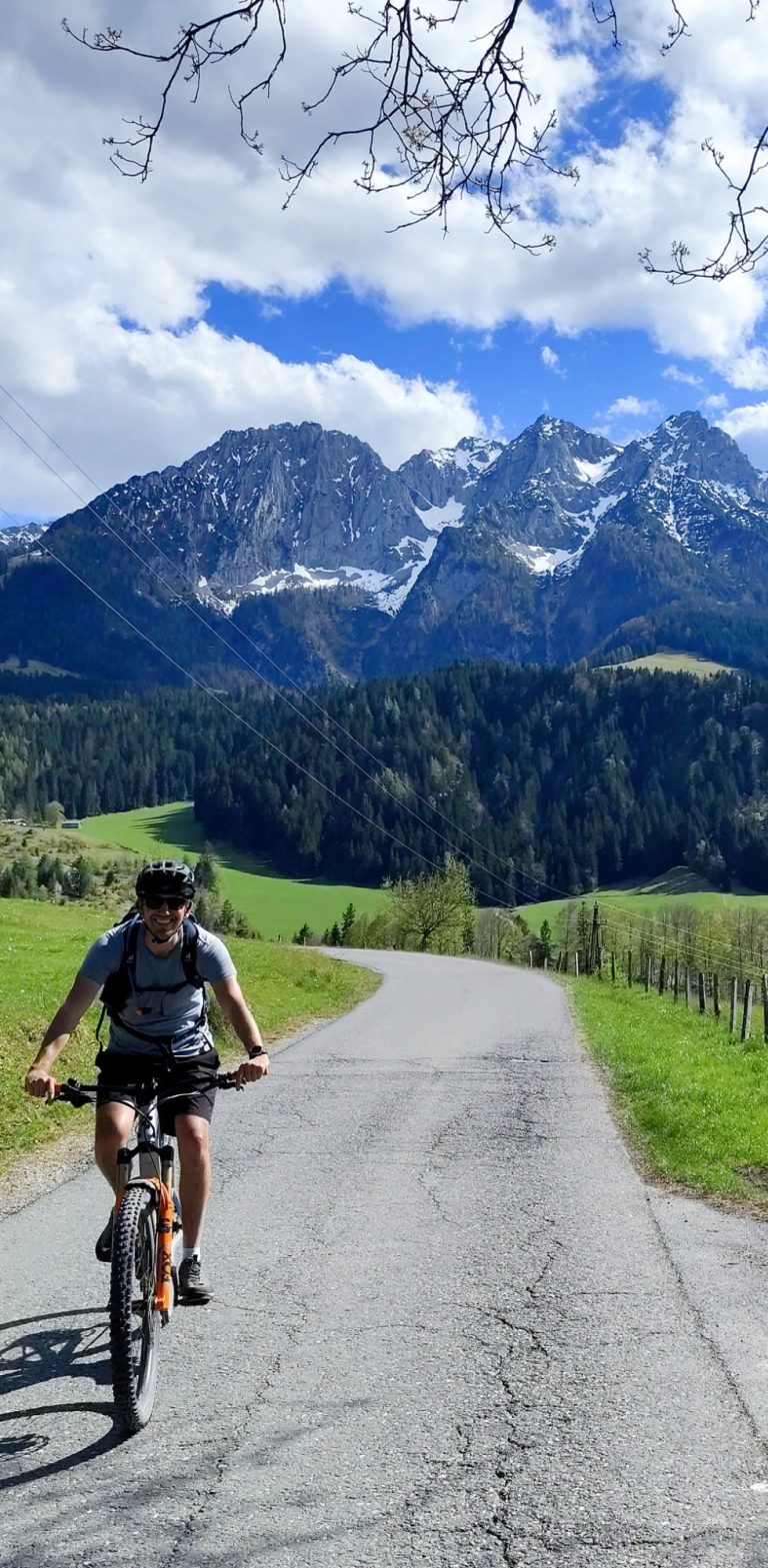 Radfahrer auf einer Straße mit Bergen und grünem Landschaftshintergrund.